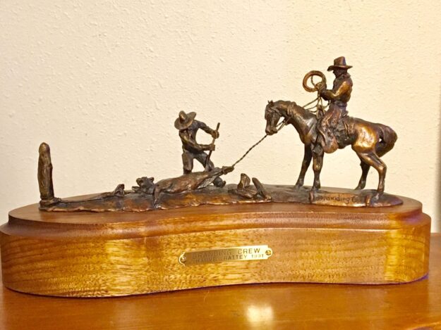 Small bronze sculpture of a cowboy on a horse and anther on the ground, branding a calf.