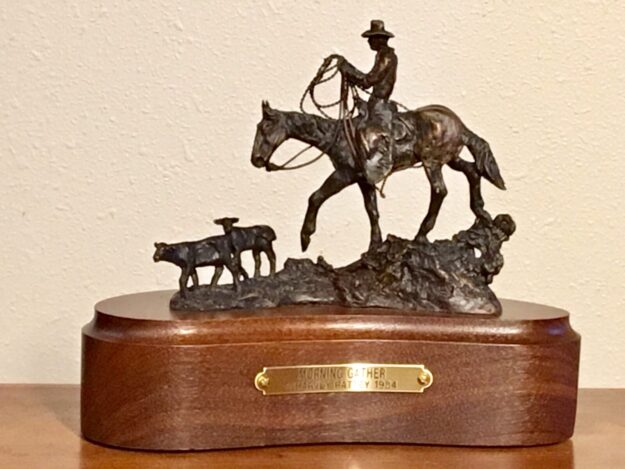 Bronze sculpture of a cowboy on his horse following two calves.