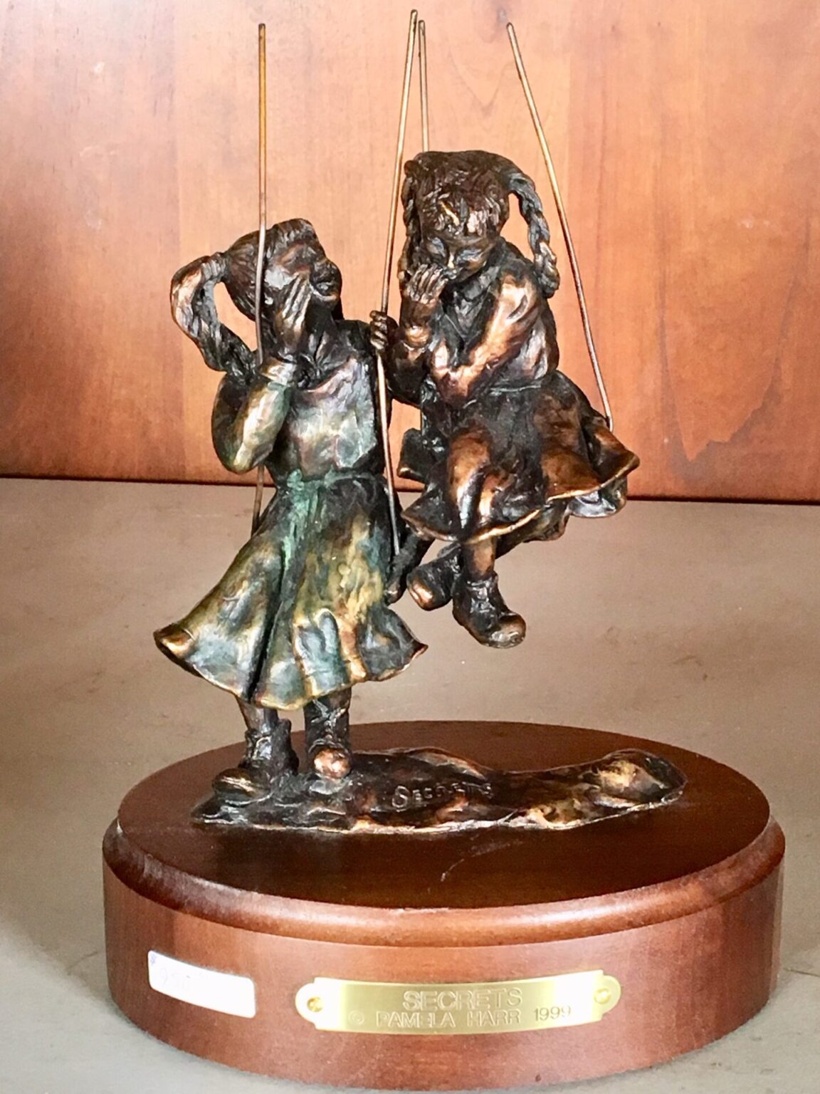 Bronze sculpture of two little girls on swings, sharing a secret.