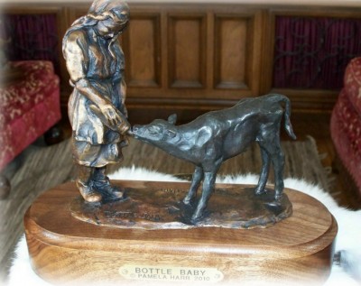 Bronze sculpture of rancher feeding orphan calf with a bottle.