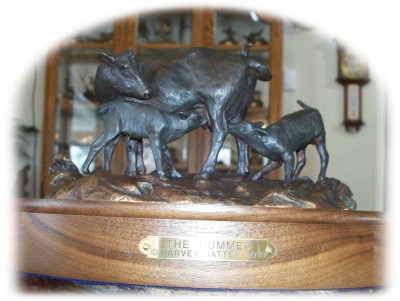 Bronze sculpture of an Angus cow nursing her calf and another calf.