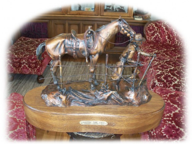 Bronze sculpture of cowboy leading his horse through a gate.