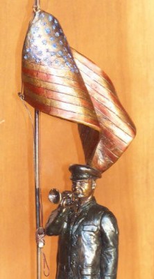 Bronze sculpture of soldier playing taps with half-mast American flag.