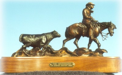 Bronze sculpture of horseback rancher bringing a calf to the barn while the cow follows.