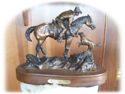 Bronze sculpture of cowboy on a horse watering his puppy