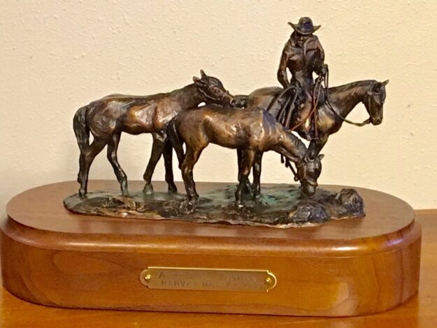 Bronze sculpture of a horseback cowboy leading two spare horses.