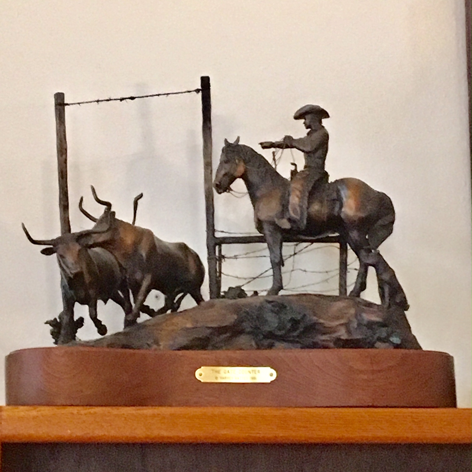 Bronze sculpture of a cowboy counting cows through a gate.