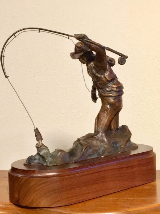 Bronze sculpture of a fly fisherman trying to land a fish.