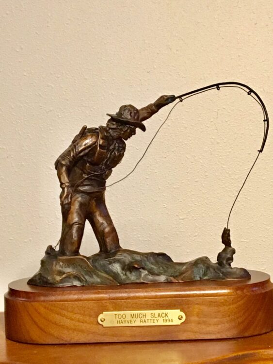 Small bronze sculpture of a fly fisherman trying to land a fish.