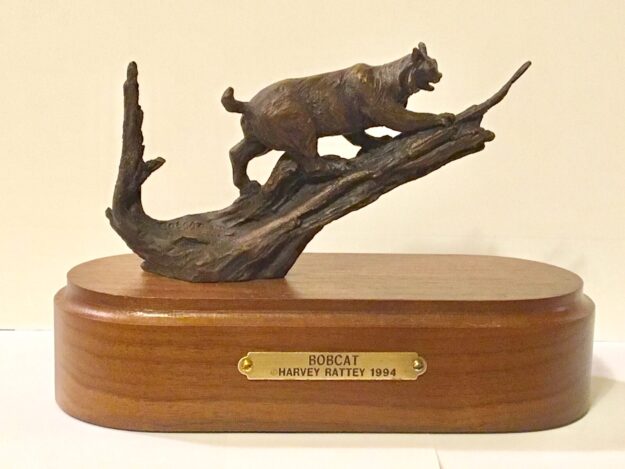 Bronze sculpture of a bobcat in a tree.