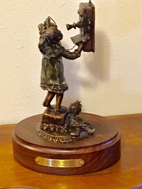 Bronze sculpture of a little girl talking on an antique telephone.