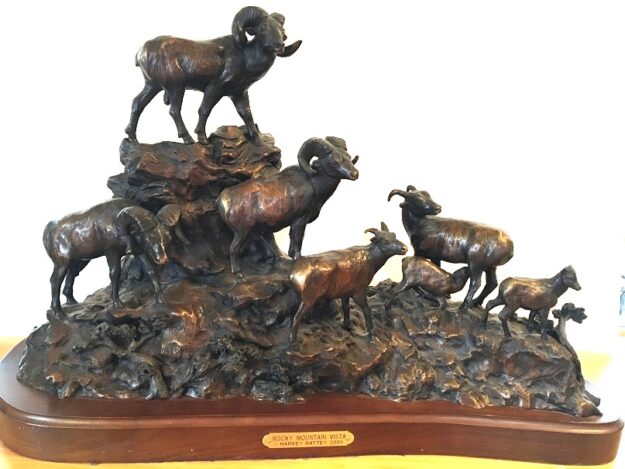 Bronze sculpture of bighorn sheep on a mountain top.