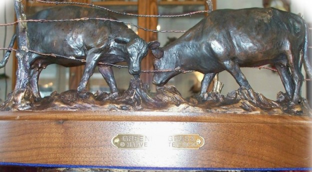 Bronze sculpture of cows grazing through the fence.