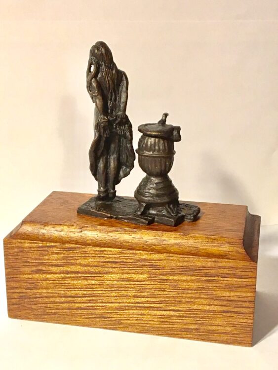 Bronze sculpture of a pioneer girl standing by a woodburning stove.