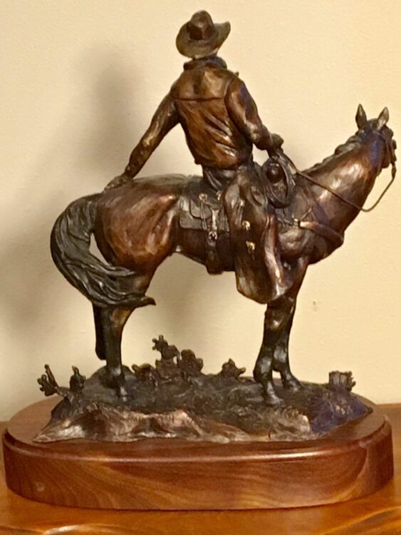 Bronze sculpture of a cowboy on his horse, facing away from the viewer.