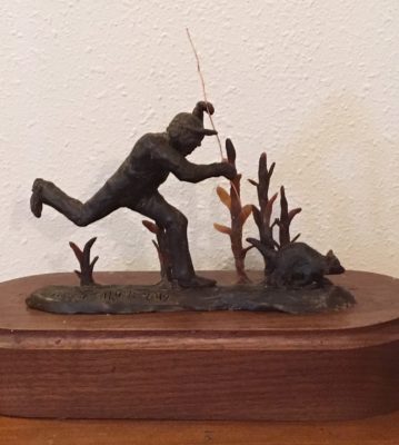 Bronze sculpture of man chasing racoon out of corn field