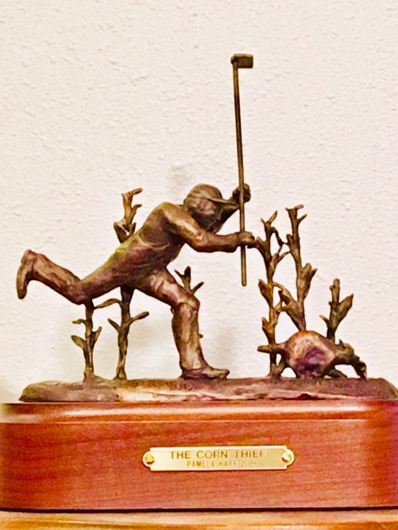 Bronze sculpture of farmer chasing a racoon out of her corn field.