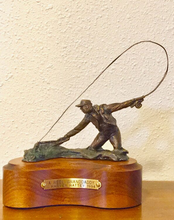 Bronze sculpture of a fly fisherman landing a big trout.