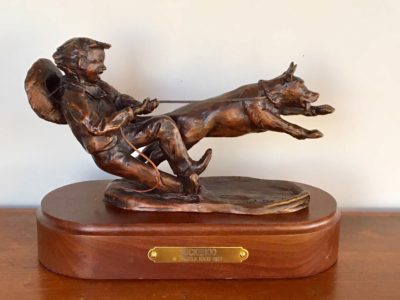 Bronze sculpture of a boy trying to hold his rambunctious dog.