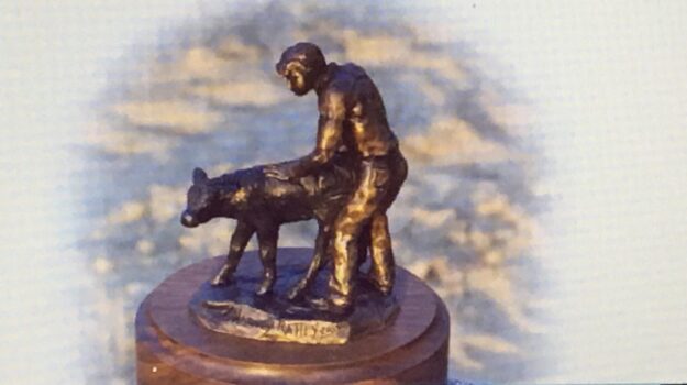 Bronze sculpture of a young boy helping a newborn calf to stand.