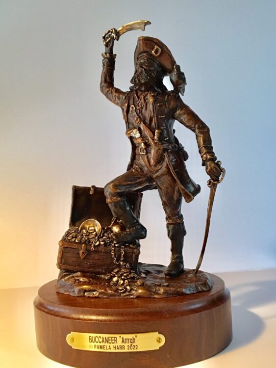 Bronze sculpture of a pirate with his cutlass raised and his foot on a treasure chest.