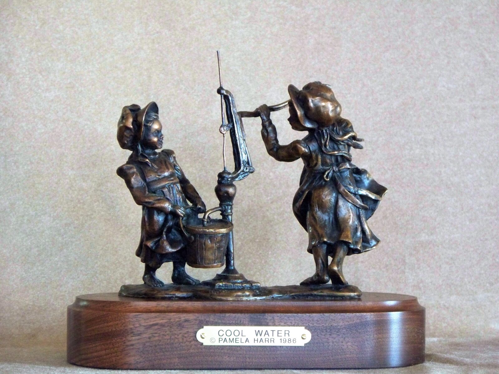 Bronze sculpture of two pioneer girls hand-pumping water into a bucket.