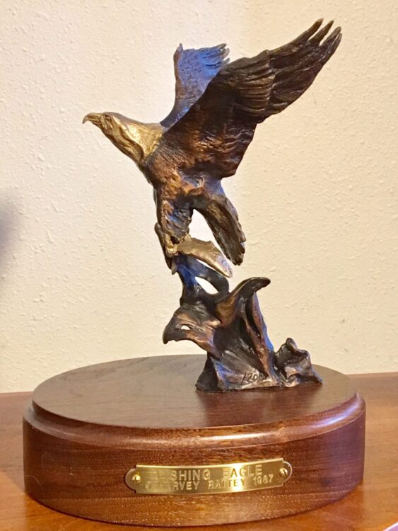 Bronze sculpture of an eagle soaring away from the water with a fish in his talons.