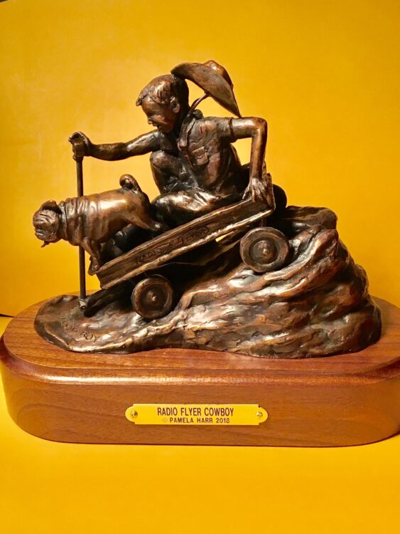 Bronze scupture of a little boy and his dog zooming downhill in a Radio Flyer wagon.