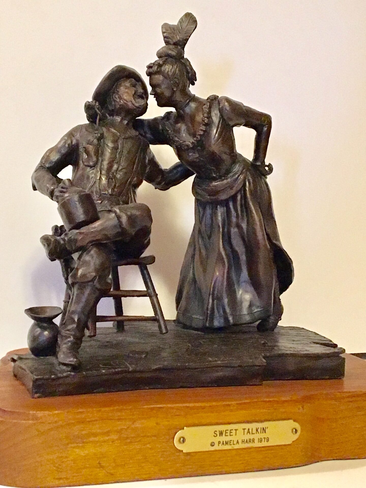 Bronze sculpture depicts a scene of a prospector on a chair with his hand on the waist of a pretty saloon girl, who is leaning in as if to give him a kiss.