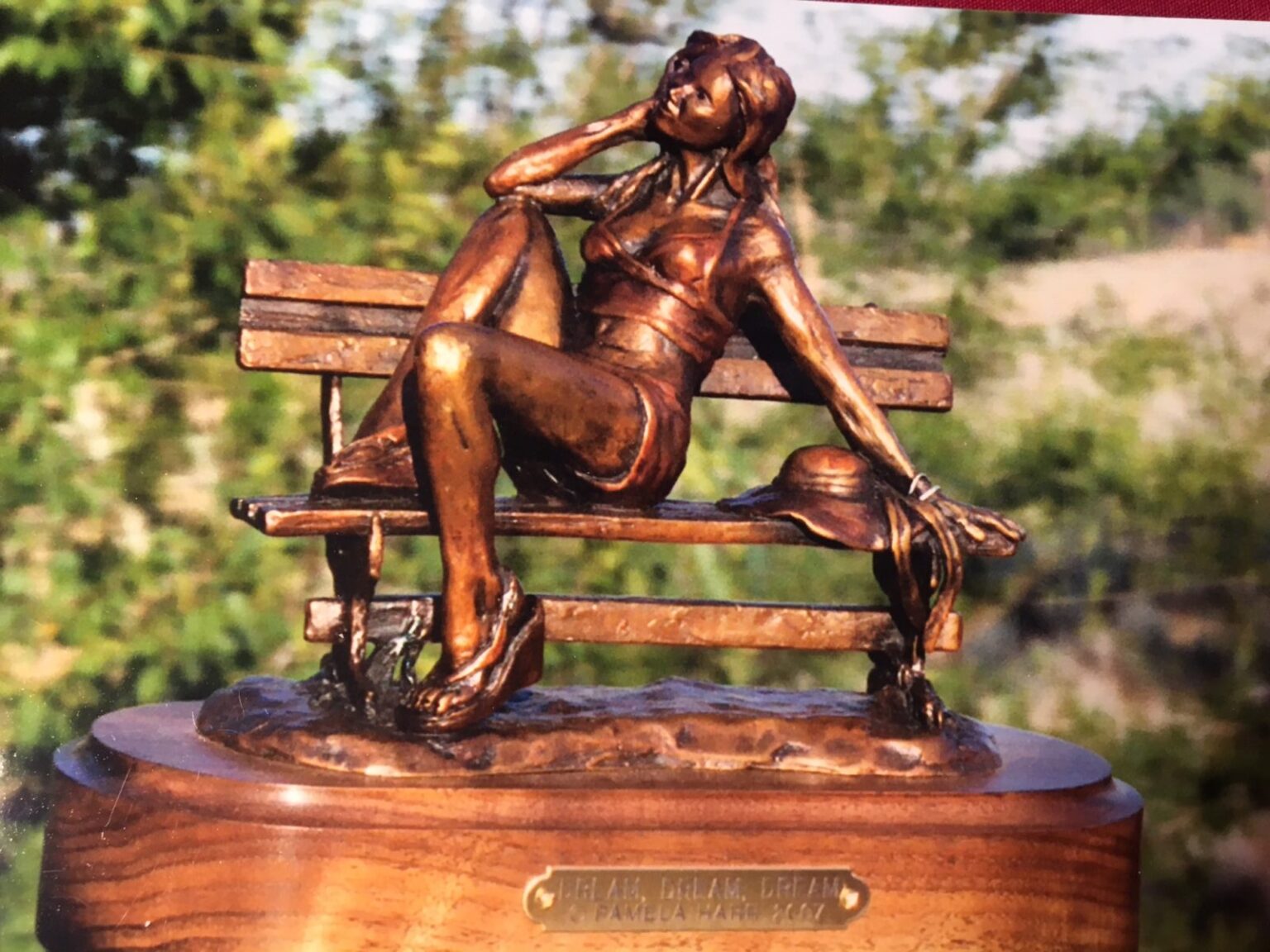 Bronze sculpture of a young woman on a park bench.