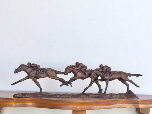 Bronze sculpture of three jockeys on race horses galloping full speed toward the finish line.