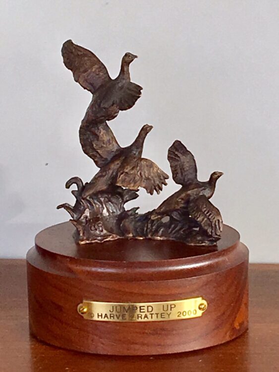 Bronze sculpture of 3 sharp-tail grouse flying up out of cover.