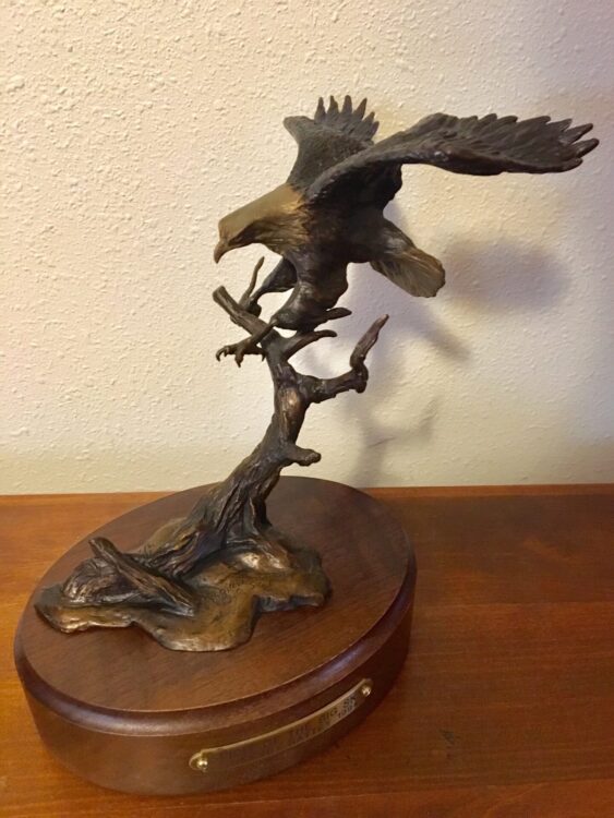 Bronze sculpture of an eagle landing in a tree.