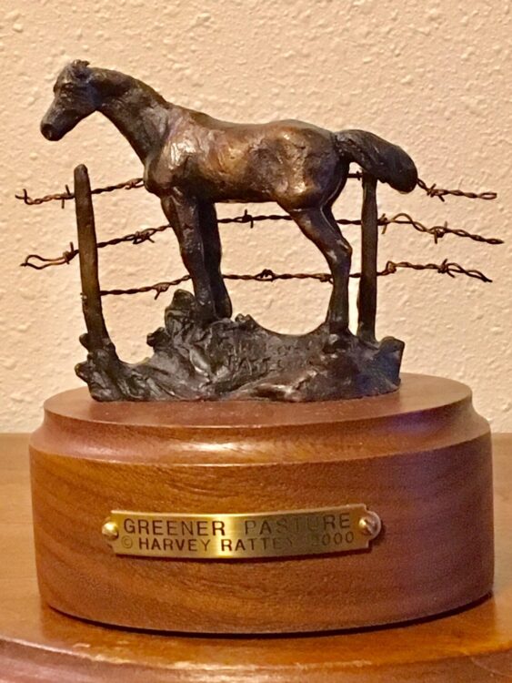 Small bronze sculpture of a horse looking over a barbed-wire fence.