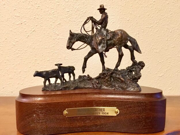 Stylized bronze sculpture of an old-time cowboy on his horse following two calves.