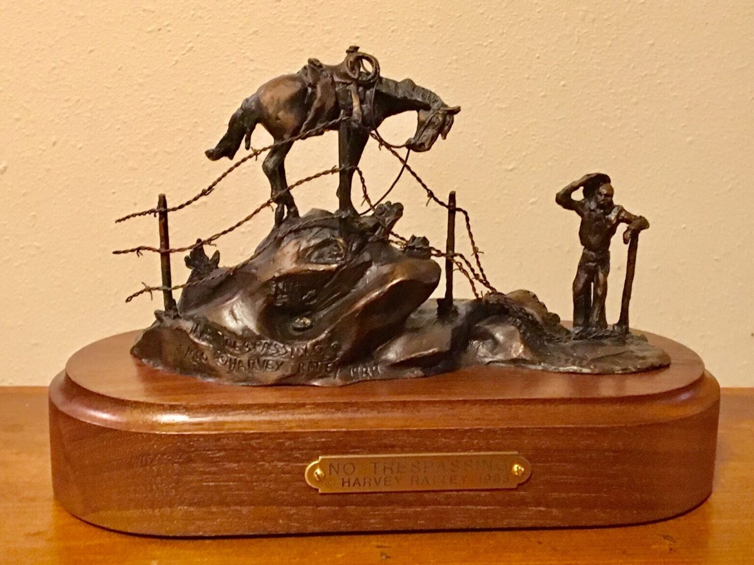 Bronze sculpture of a cowboy (with his horse) looking at evidence of someone disregarding his 'No Trespassing' sign.